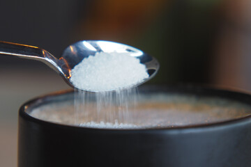 white sugar pouring from a in a paper packet on a coffee cup 