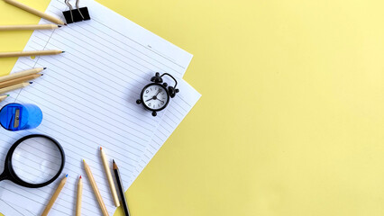 Top view pencil color, pencil, alarm clock, magnifying glass, paper clip, sharpener and paper on yellow background