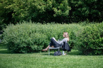 Serene woman deeply engaged in book, sprawled on chair in park. Break from city chaos and digital...
