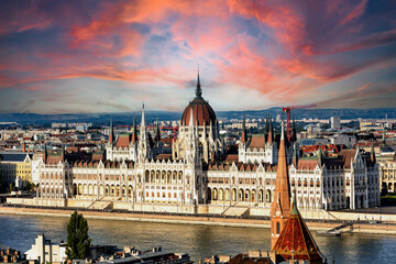 Obraz premium Sunset view of Budapest, highlighting the historic Parliament, Danube River, and iconic landmarks like Buda Castle and Chain Bridge. Perfect for showcasing Hungary’s stunning architecture and vibrant