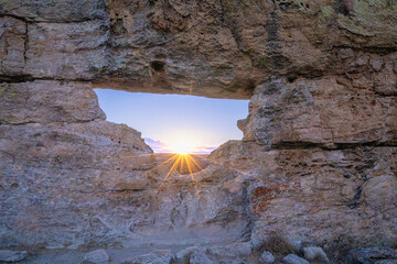 Spectacular sunburst piercing through natural rock formation with multicolored lichen patterns. Famous Window of Sunset viewpoint at Isalo National Park, Madagascar.