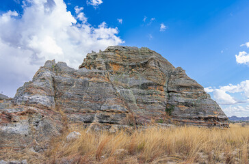 Iconic Queen of Isalo sandstone rock formation with distinctive crown-like top under dramatic cloudy sky. Natural weathered limestone cliffs surrounded by grass. Isalo National Park, Madagascar.