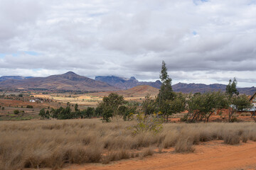 Fototapeta premium Expansive farmland with patches of green and brown fields under a cloudy sky. Rural landscape, Isalo National Park, Madagascar.