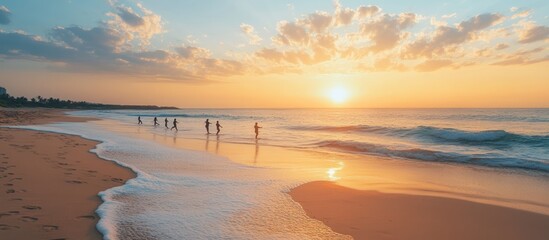 Silhouettes of people walking along a sandy beach at sunset with waves crashing on the shore.