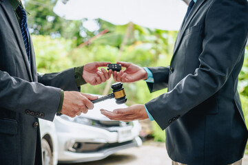 An Asian businessman buys a car, signs a contract with the salesman, and receives the keys. They discuss essential terms, covering car leasing, finance, and loan laws to finalize the purchase