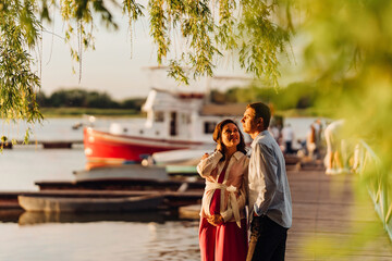 man and pregnant woman in red dress at sunset on the pier 