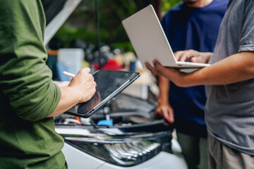 Asian clients engage with a car insurance agent beside a wrecked vehicle. They examine the policy details, assess the damage, and finalize paperwork related to the insurance claim and repairs.