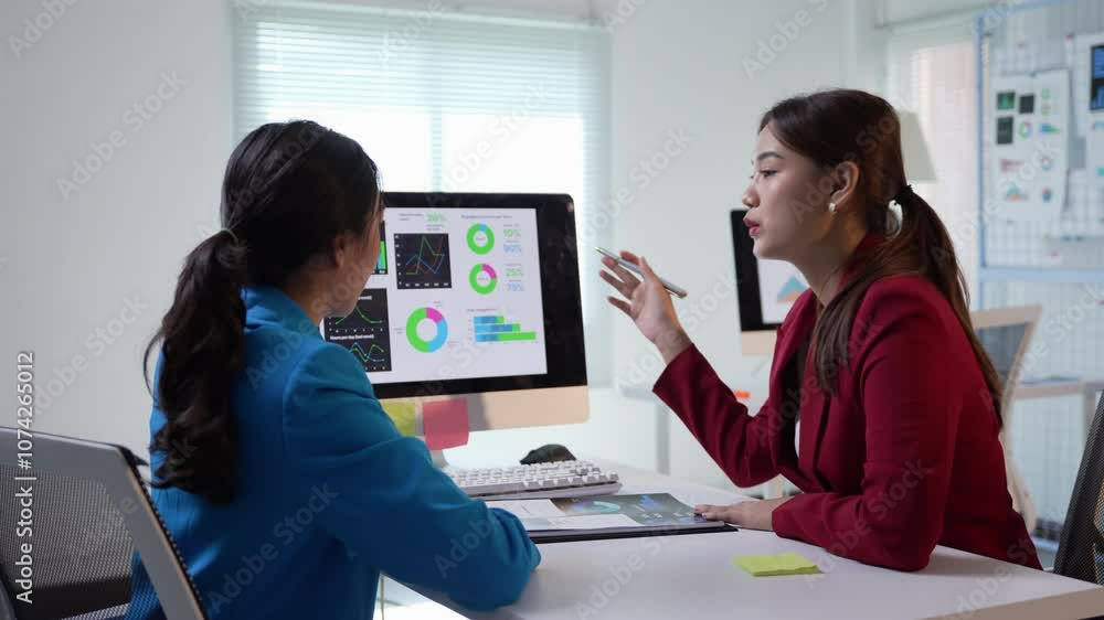 Poster two businesswomen engage in a productive conversation while using a computer in a modern office sett