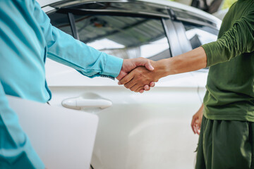 Asian clients engage with a car insurance agent beside a wrecked vehicle. They examine the policy details, assess the damage, and finalize paperwork related to the insurance claim and repairs.