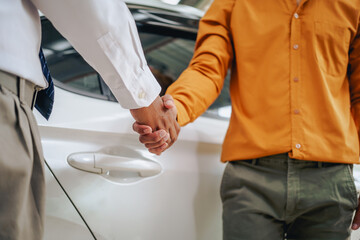 Asian clients engage with a car insurance agent beside a wrecked vehicle. They examine the policy details, assess the damage, and finalize paperwork related to the insurance claim and repairs.