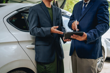 Asian clients engage with a car insurance agent beside a wrecked vehicle. They examine the policy details, assess the damage, and finalize paperwork related to the insurance claim and repairs.