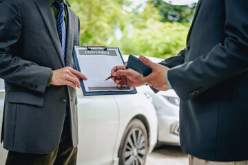 Asian clients engage with a car insurance agent beside a wrecked vehicle. They examine the policy details, assess the damage, and finalize paperwork related to the insurance claim and repairs.