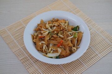plate of stir-fried noodles with vegetables, bean sprouts, and chili slices, served on a bamboo mat