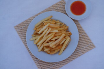 crispy French fries is served with a side of red dipping sauce on a bamboo mat