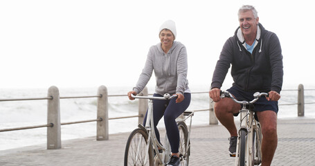 Senior couple, bicycle and happy on promenade, beach and outdoor in morning with exercise in summer. Man, woman and cycling with smile by sea, ocean and journey for workout with bonding in England