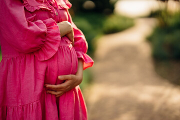 pregnant woman in pink dress hugging belly in the park