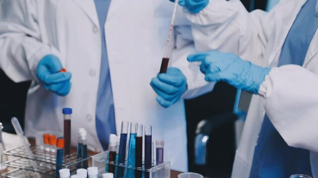 Group of dedicated scientist conduct chemical experiment in medical laboratory, carefully drop precise amount of liquid from pipette into test tube for vaccine drug or antibiotic development. Neoteric