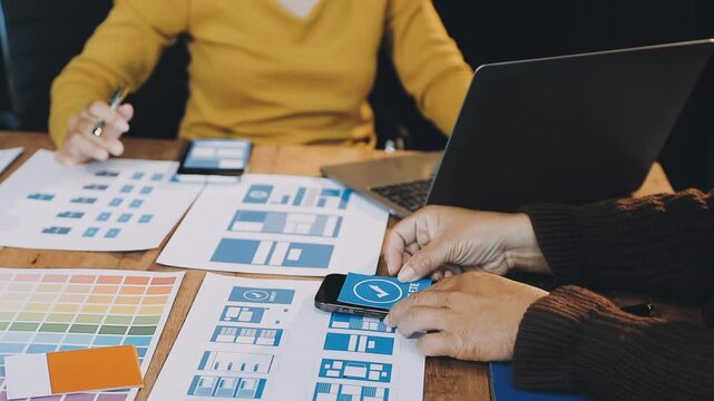 Web design process. The web designer creating a mockup of the mobile application according to the customer's brief. Samples and sketches laying at the table