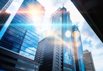 A low angle view of tall skyscrapers with a bright, sunlit sky.