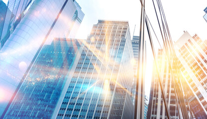 A low angle view of a city skyline with tall buildings and bright sunlight reflecting off the glass windows.