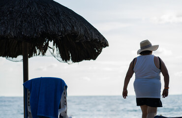 mujer mayor con sombrero de espaldas caminando en la playa en vacaciones 