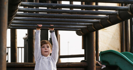 Boy, child and swing on monkey bars at playground, outdoor or adventure with lifting, learning and balance. Kid, memory and exercise on jungle gym at park for challenge, climbing or sunshine in Spain