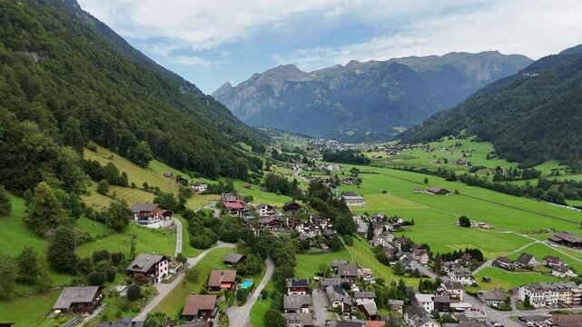 Aerial orbit wide shot of swiss village during idyllic landscape in fall season. Main street with apartments and homes and alps in background. Establishing shot.