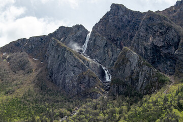 At the top of a towering cliff in Gros Morne, a small waterfall cascades gracefully, enhancing the serene beauty and rugged charm of this iconic national park.