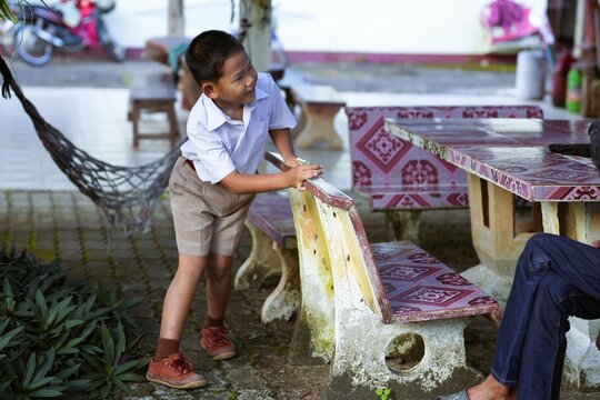 Asian boy wearing school uniform running around the table