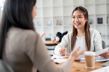 Two females talking and discussing, doing paper work  at office desk.