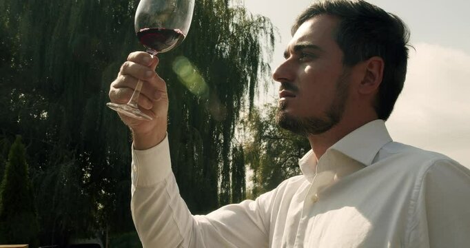 Man winemaker tasting wine. Sommelier is shaking the glass of wine and tasting it. Elegantly dressed man is tasting a flavor and drinking fresh red wine poured in transparent glass.