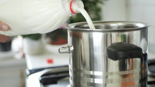 Shooting with a Person in the Kitchen Putting Fresh Milk from a Bottle in the Pot for Boiling. 