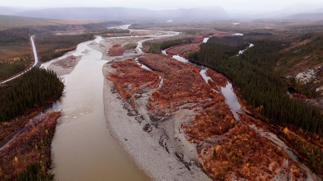 Ogilvie River Flowing Along The Dempster Highway, Mountain And Forest During Autumn On A Foggy Morning In Yukon, Canada. - aerial shot