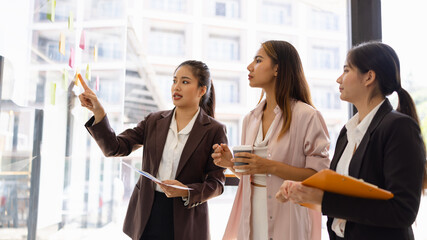 Asian businesswoman teamwork planning with sticky notes and new ideas on a glass wall, Business...