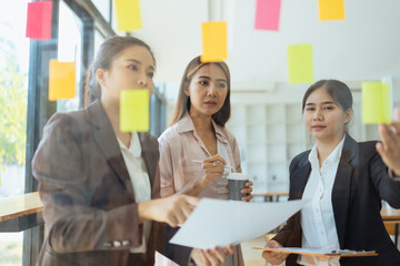 Asian businesswoman teamwork planning with sticky notes and new ideas on a glass wall, Business people brainstorming strategy and new ideas concept, startup worker meeting,