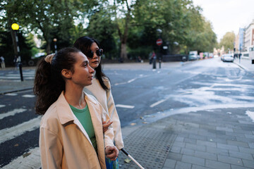 Blind woman holding white cane crossing street with friend in london
