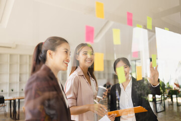 Asian businesswoman teamwork planning with sticky notes and new ideas on a glass wall, Business people brainstorming strategy and new ideas concept, startup worker meeting,