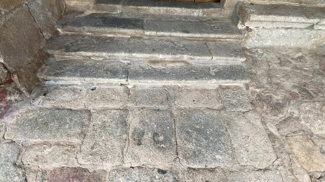 We see an old very worn white granite stone floor, a few steps away from it appears a spectacular large two-leaf wooden door, medieval style with its decorative iron studs, it is in slow motion