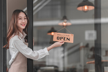 Young woman cheerfully opens her cafe with a warm welcome sign to customers