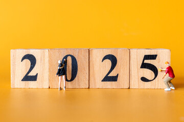 Miniature figures in overalls paint and construct the numbers 2025 on wooden blocks