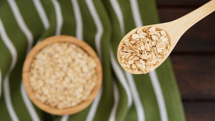 Wooden spoon with oats on green striped cloth background, highlighting natural, healthy food...