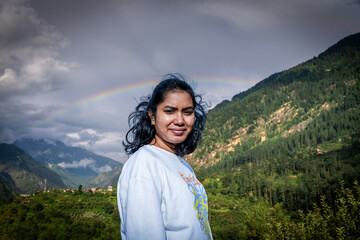 Young Indian woman enjoying her vacation and admiring the mountain landscape with a rainbow