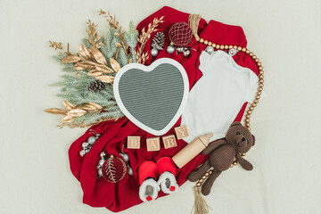 Holiday pregnancy announcement with baby onesie, cozy slippers, and teddy bear arranged on a festive background. Ideal for Christmas, winter celebrations, or baby arrival themes.