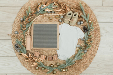 Festive baby announcement setup featuring a baby onesie, a letterboard, and seasonal holiday...