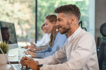 Portrait of call center worker accompanied by his team. Smiling customer support operator at work.