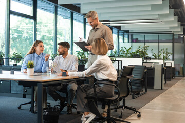 Handsome man gesturing and discussing something while his coworkers listening to him sitting at the...