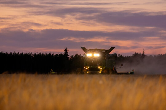 Spirit River, Alberta, Canada - August 28, 2024: John Deere s780 combine is working late in the evening with headlights, wheat field and red and purple sunset.