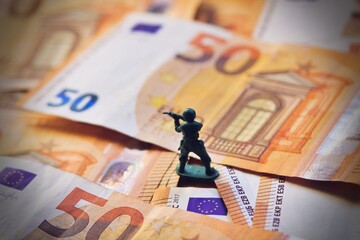 Toy soldier on Euro bills banknotes, war costs concept.