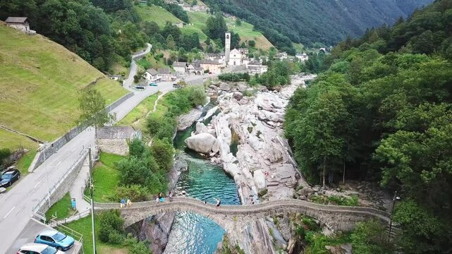 Aerial view of the birdge and the river in the town of Lavertezzo, Ticino, Switzerland; with a main road on the side, greenery and a few car passing by.