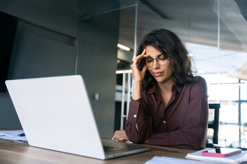 Focused young businesswoman looking at laptop pc computer screen having headache, migraine. Latin...